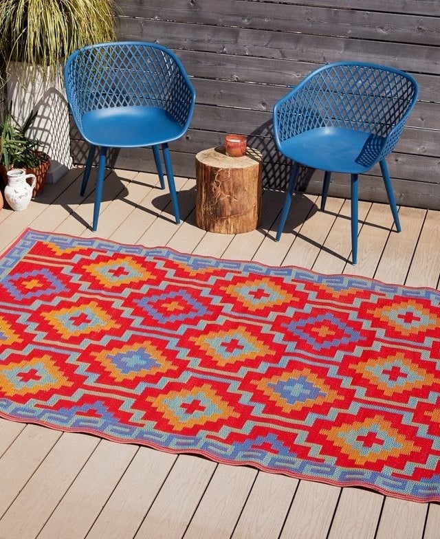 The red and blue rug is displayed outside next to some patio chairs