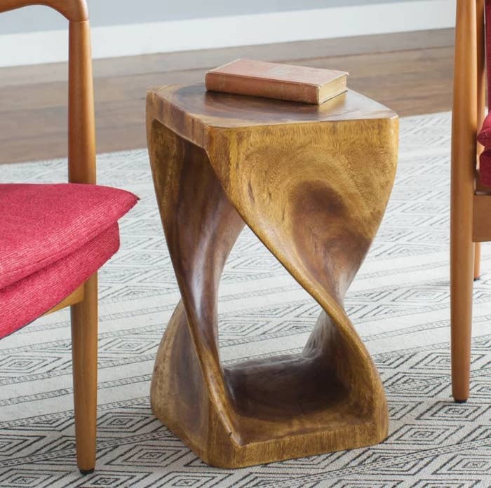 A solid wood, abstract end table next to an accent chair with a book on top