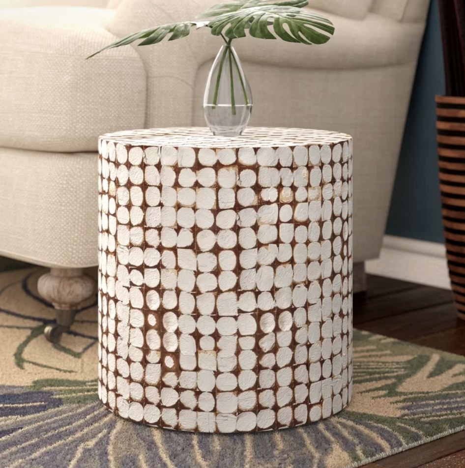 A white, solid wood drum end table with a planter on top displayed in a living room next to a couch