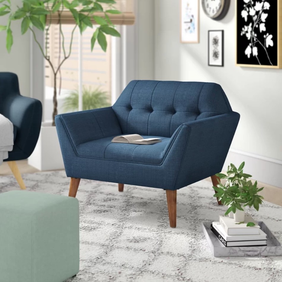 A 100% polyester, blue tufted armchair on a carpet in a living room with a book on it