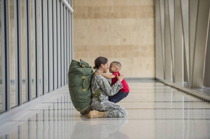Female veteran returning from war in fatigues hugging her son.