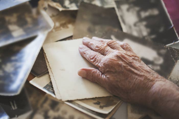 An older person's hand sits on top of a stack of papers and photographs