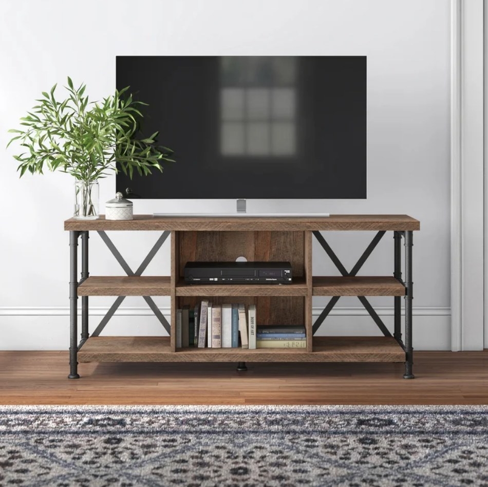 A 60-inch, wood tv stand with six shelves displayed under a tv filled with some books and a cable system