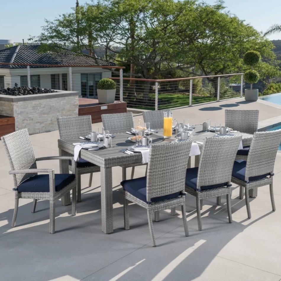 An eight-person, grey dining set with navy cushions on a patio outside