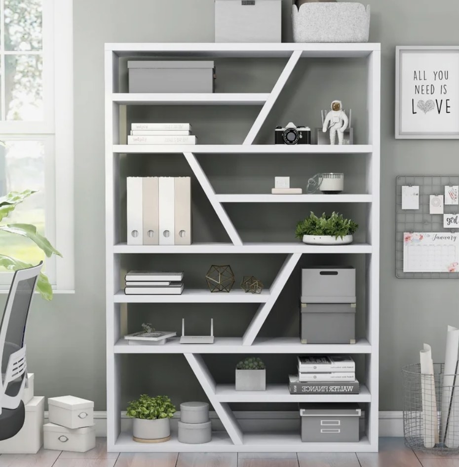 A 70.75&#x27;&#x27; H x 47.25&#x27;&#x27;, white geometric bookcase filled with books, filing boxes, plants, and other decor pieces