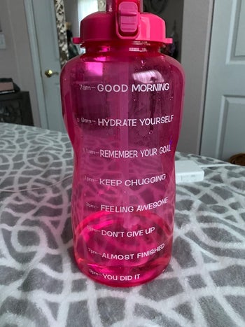 the gallon water bottle in pink that has positive messaging at each water marker that reads good morning hydrate yourself remember your goal keep chugging and more