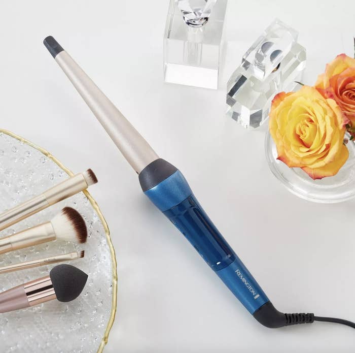 A blue heat-styling tool, makeup brushes and orange roses