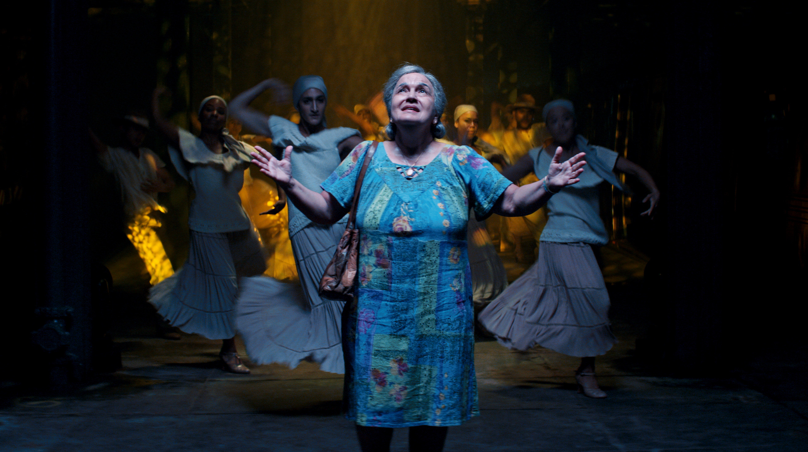 Abuela in a tunnel with people dancing behind her