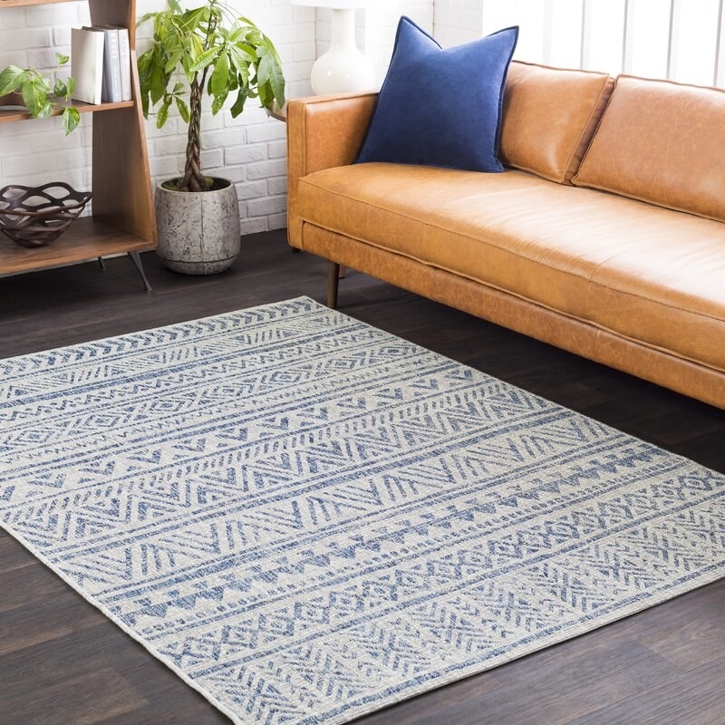 rectangular blue and grey chevron patterned area rug in front of tan couch