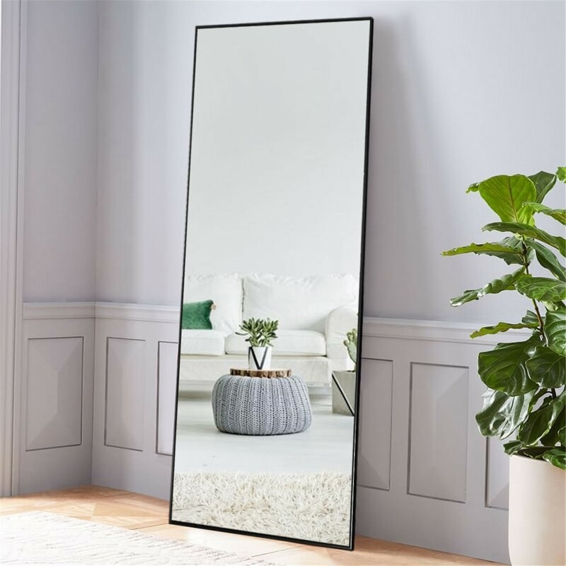 rectangular floor mirror with black frame against a wall
