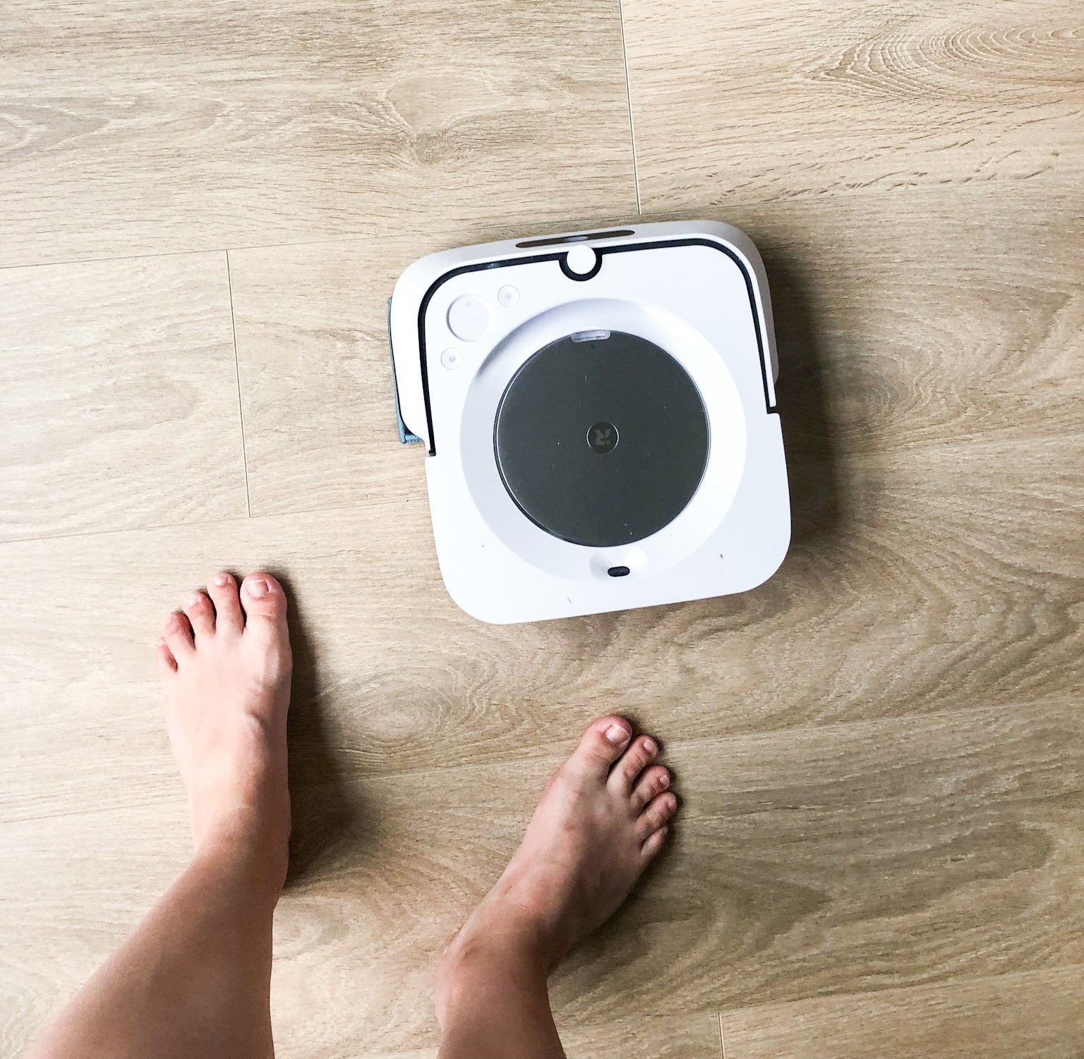 The robot mop cleaning a hardwood floor; two feet are visible for size reference