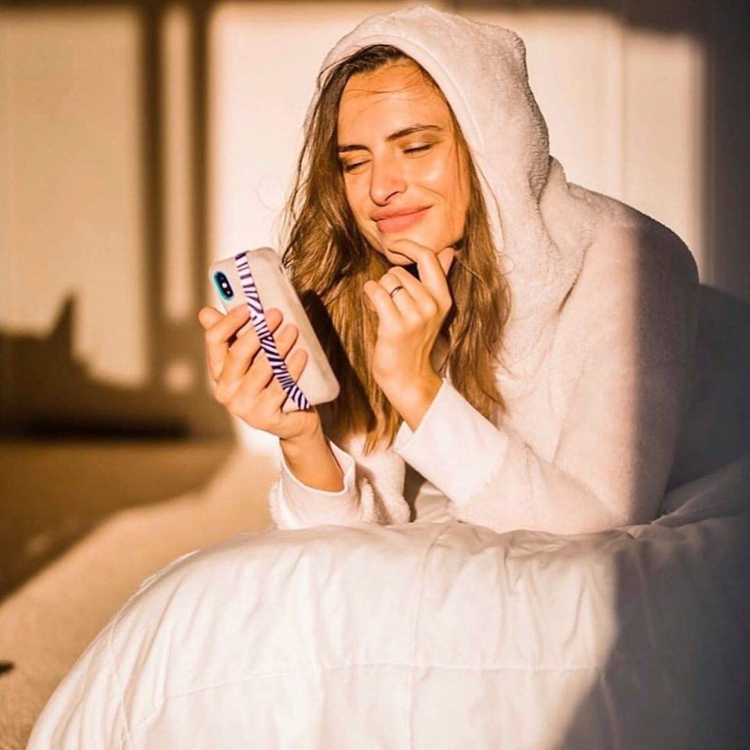 A person lying on their bed using their phone The phone has a long strap along the back