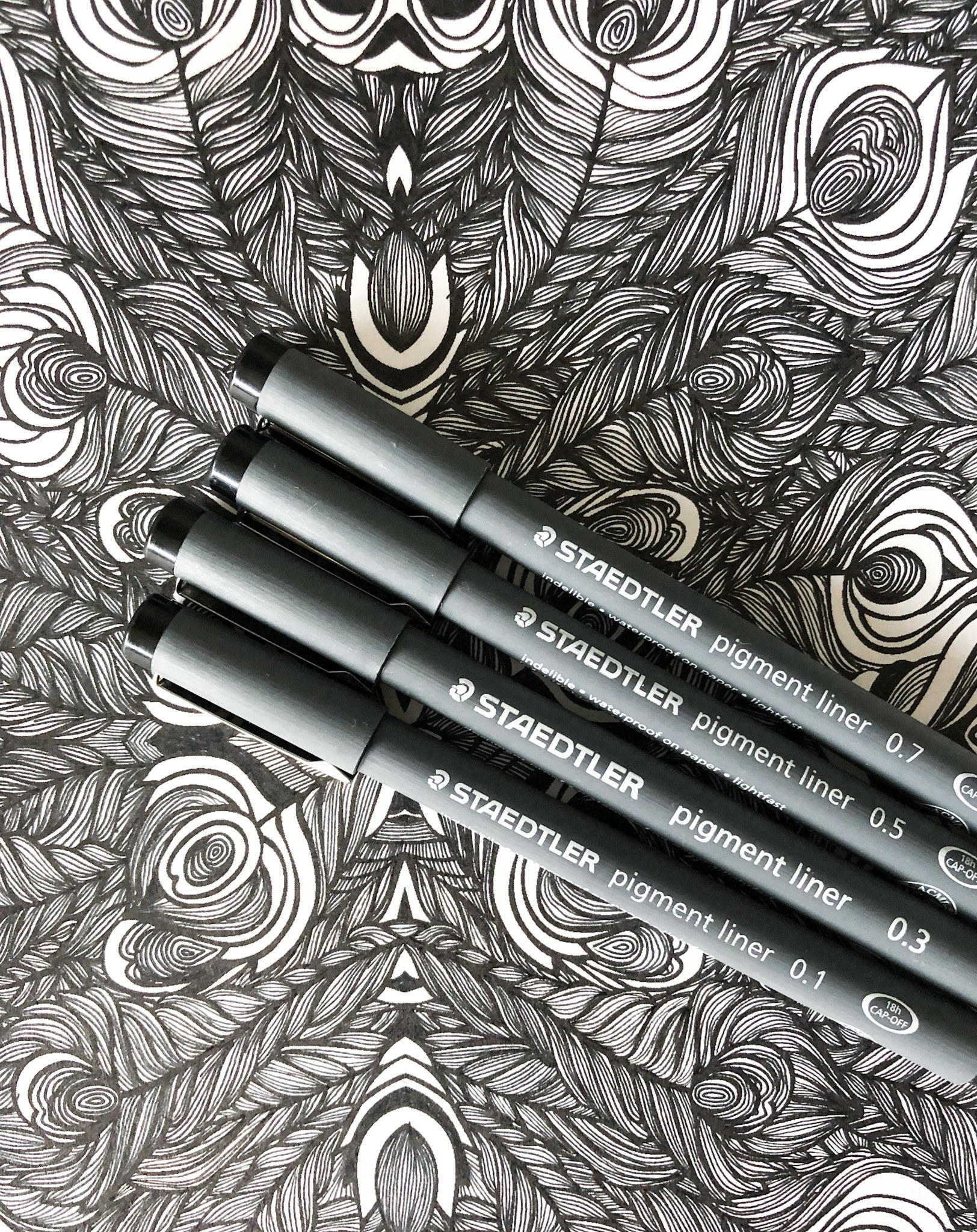 A flatlay of four sketching pens laid on a black and white line drawing