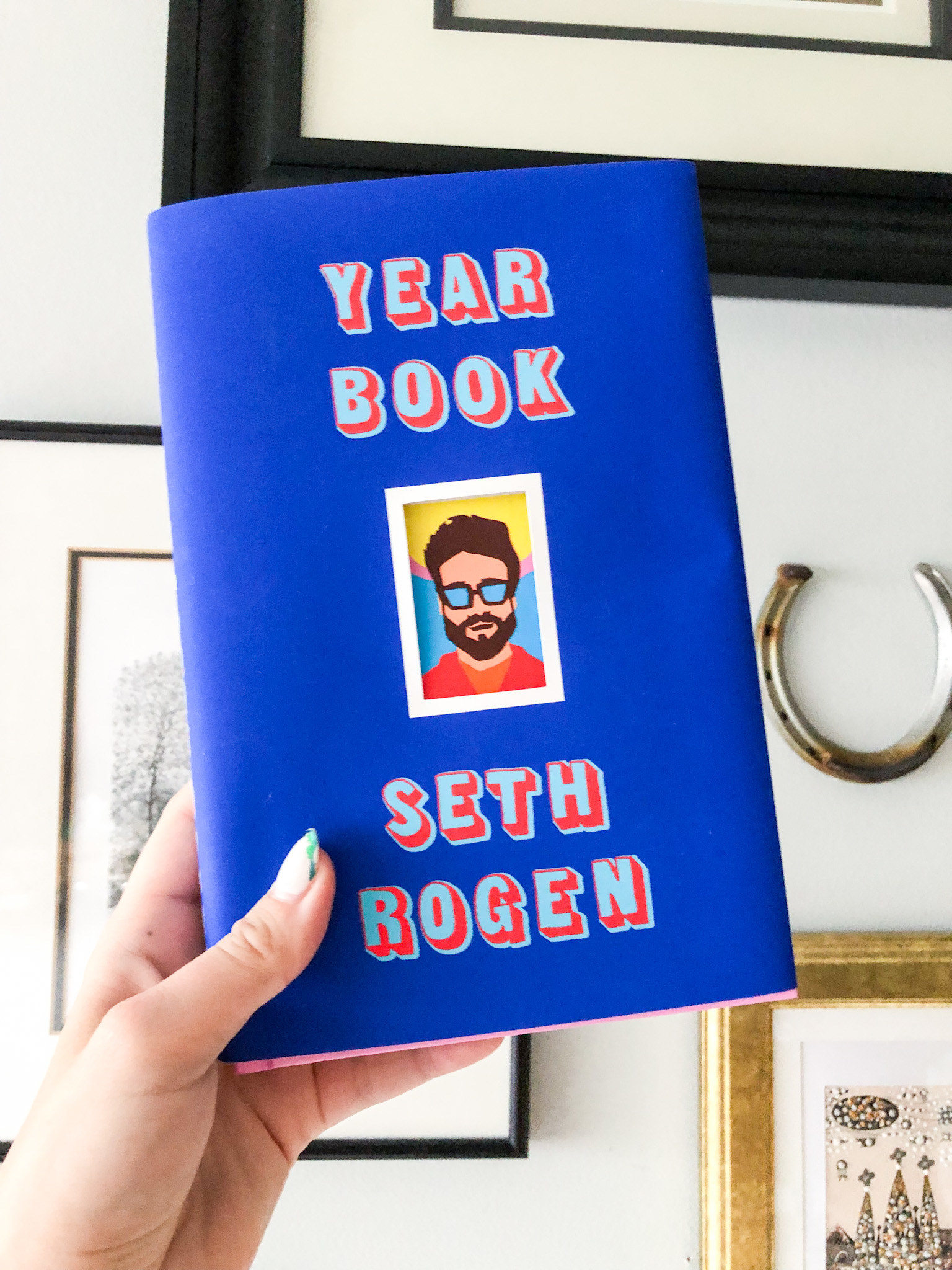 Someone holding up Seth Rogen&#x27;s book, Yearbook, against a gallery wall