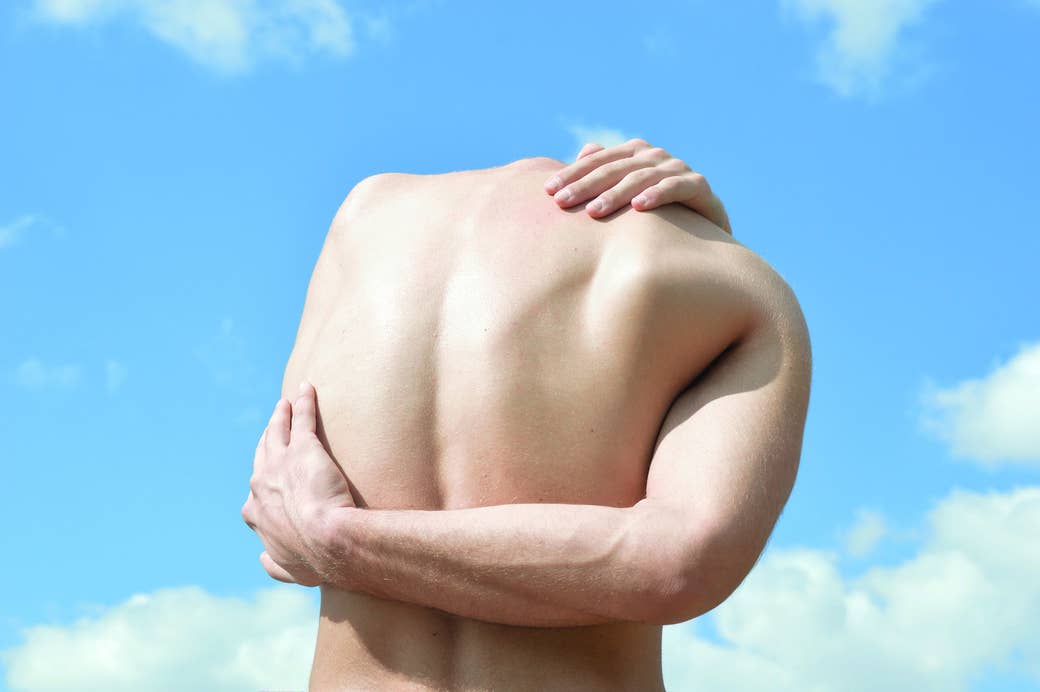 A man wraps his arms around his back in front of a blue sky