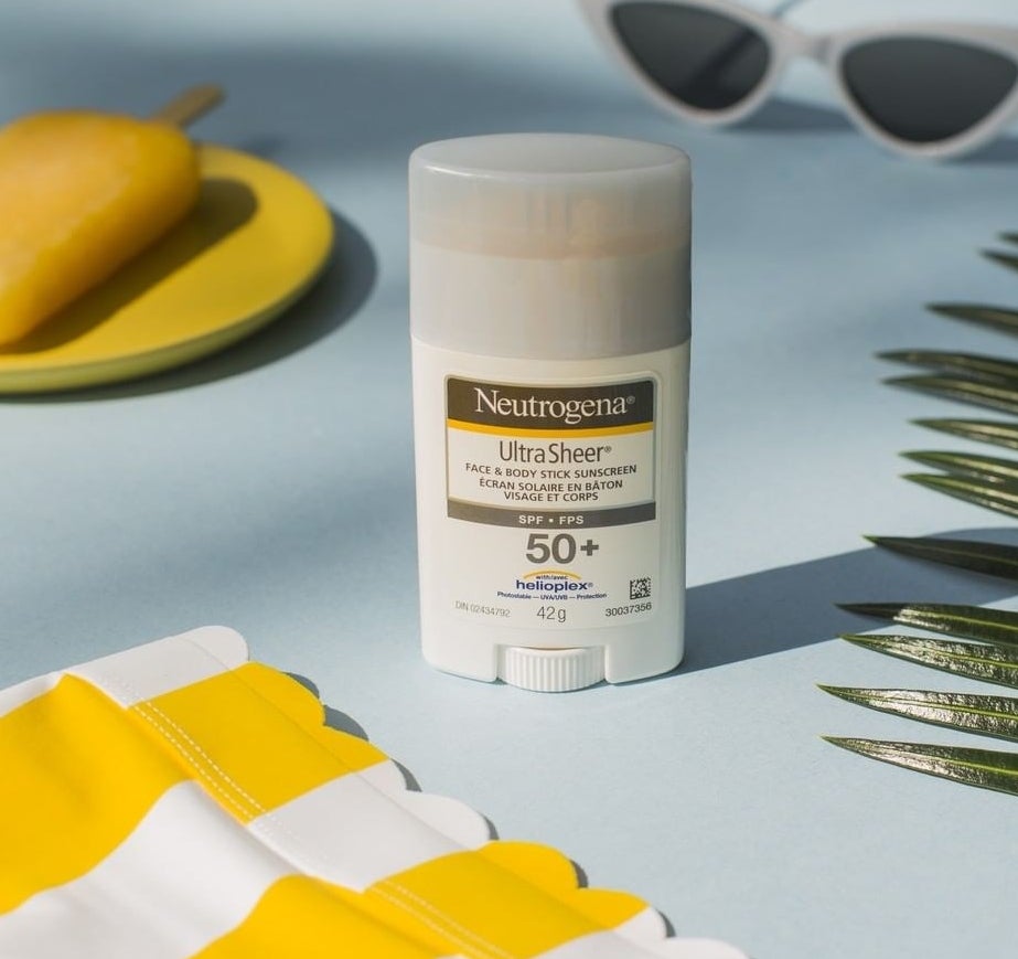 A stick of Neutrogena sunscreen on a table surrounded by sunglasses, a leaf, and a tablecloth