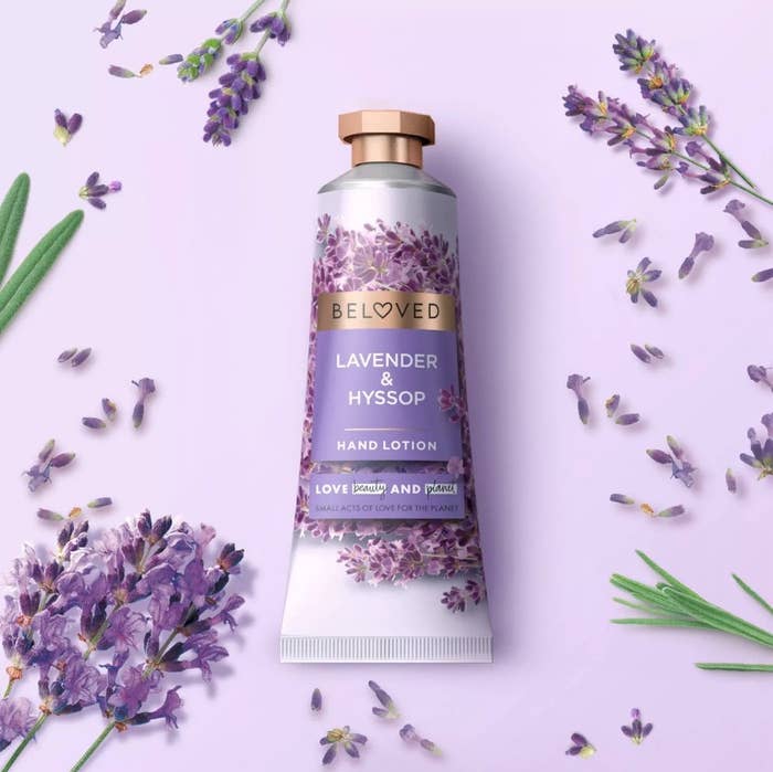 A bottle of Beloved hand cream in lavender & hyssop scent laying on lavender petals