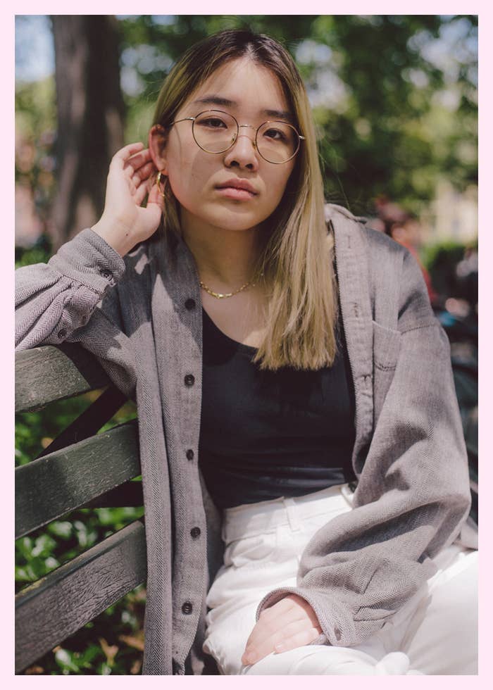 A woman in glasses and an oversized shirt sitting on a park bench looking at the camera