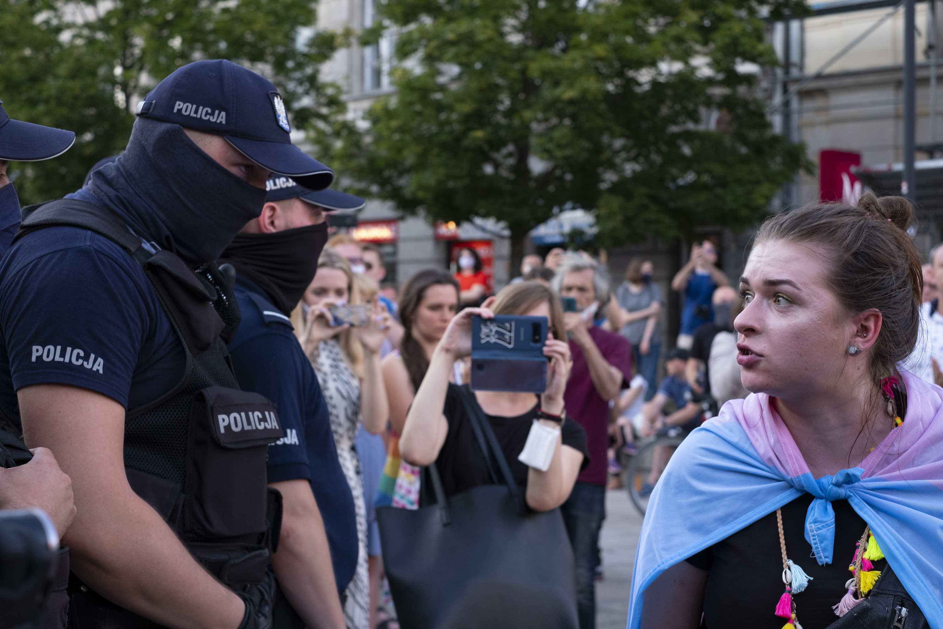 A protester talks to a line of police officers while onlookers capture it with their smartphones