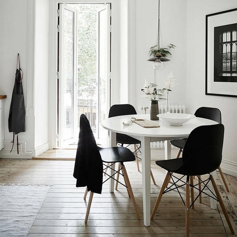 four black modern plastic dining chairs with wood legs around a round white table