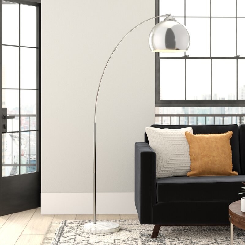 silver arched floor lamp with bell-shaped shade and marble base next to a black couch