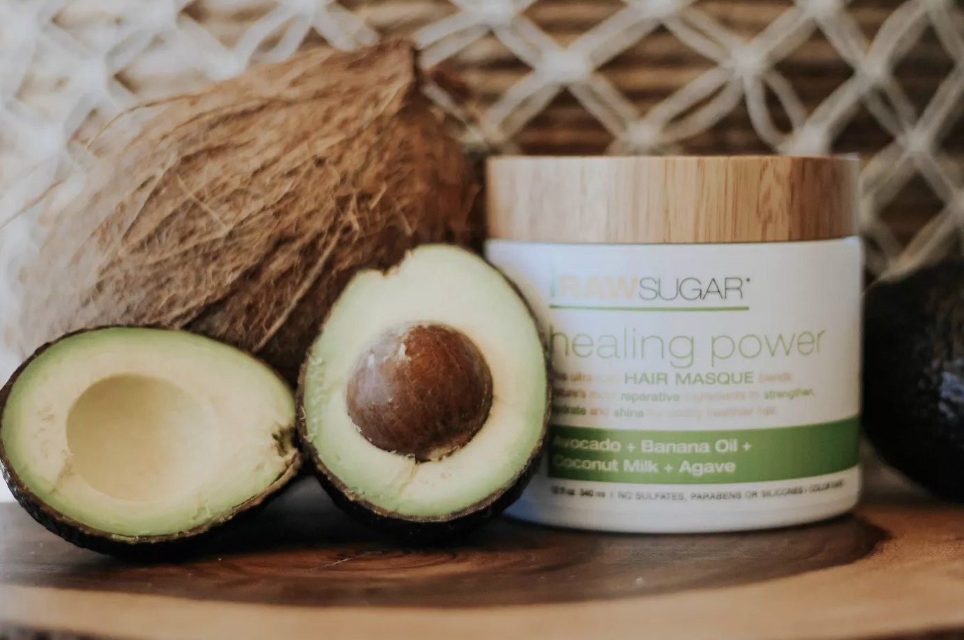 A jar of hair mask with a cut avocado and a whole coconut