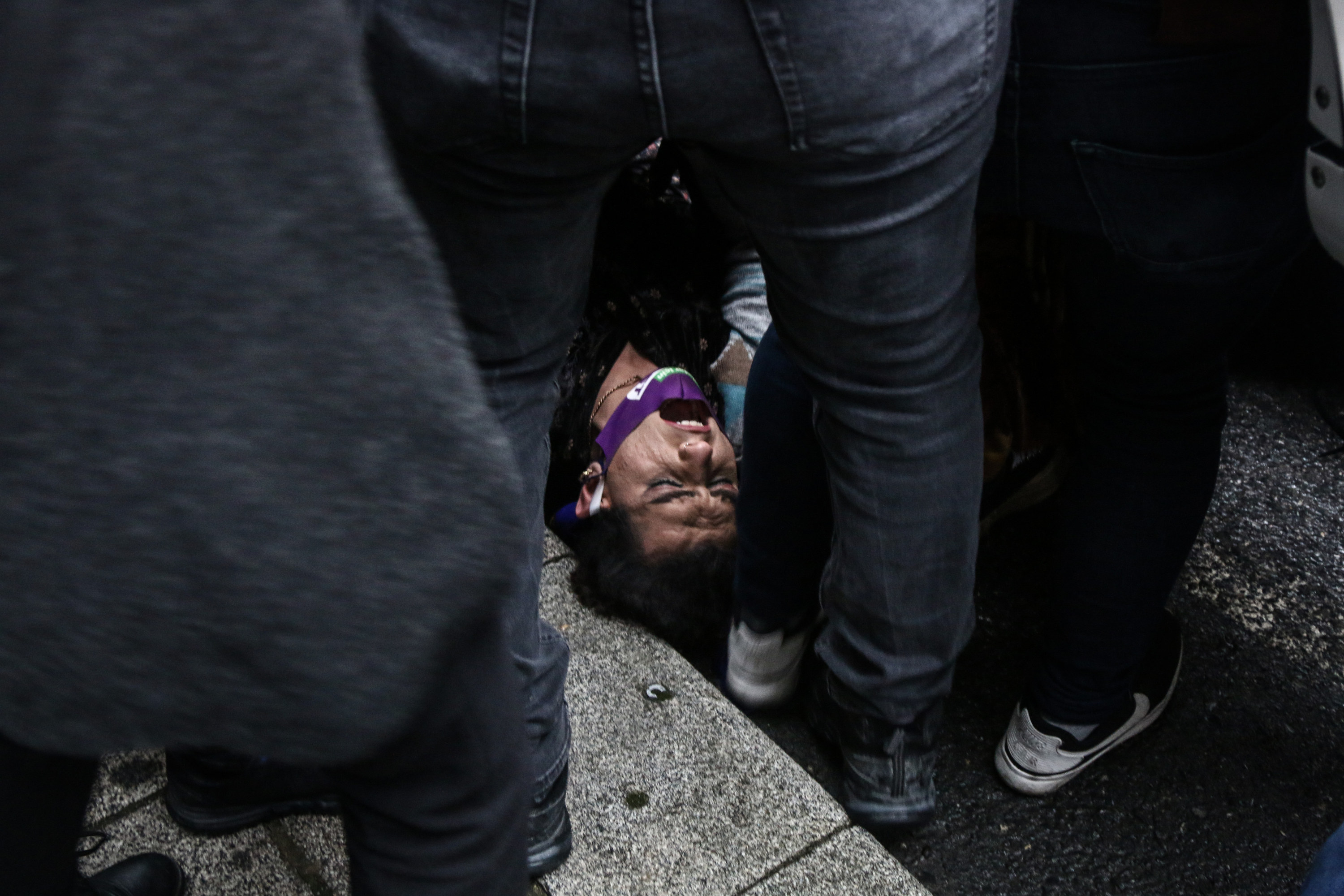 An activist shouts while lying on the ground, surrounded by other people standing