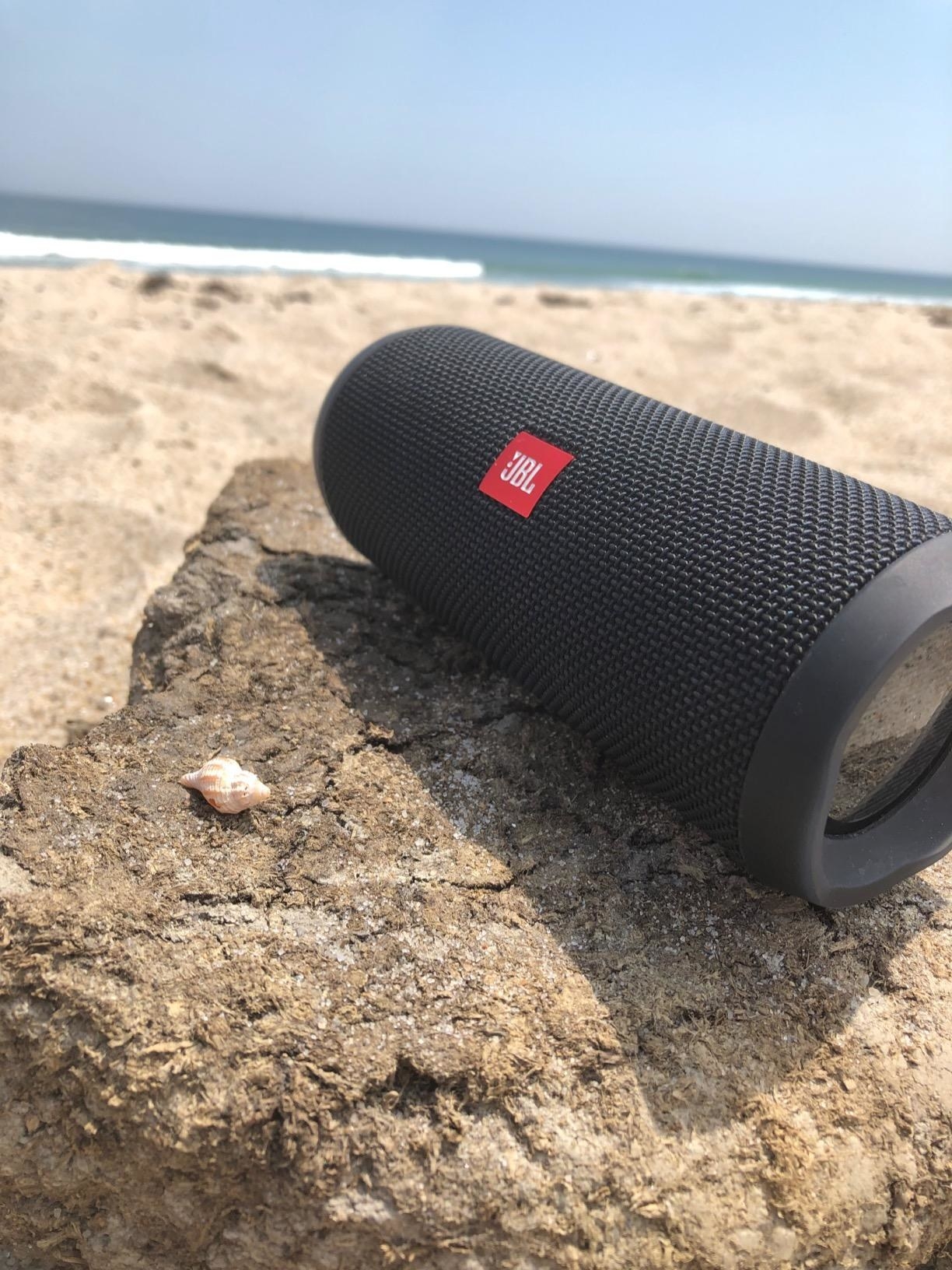 reviewer photo of a JBL black portable waterproof speaker at the beach