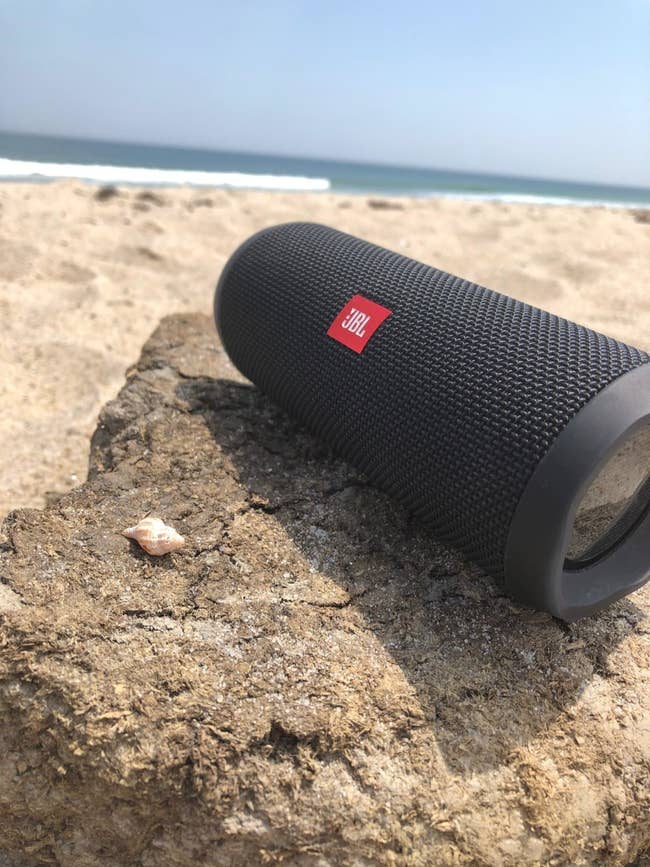 reviewer's JBL black portable waterproof speaker at the beach