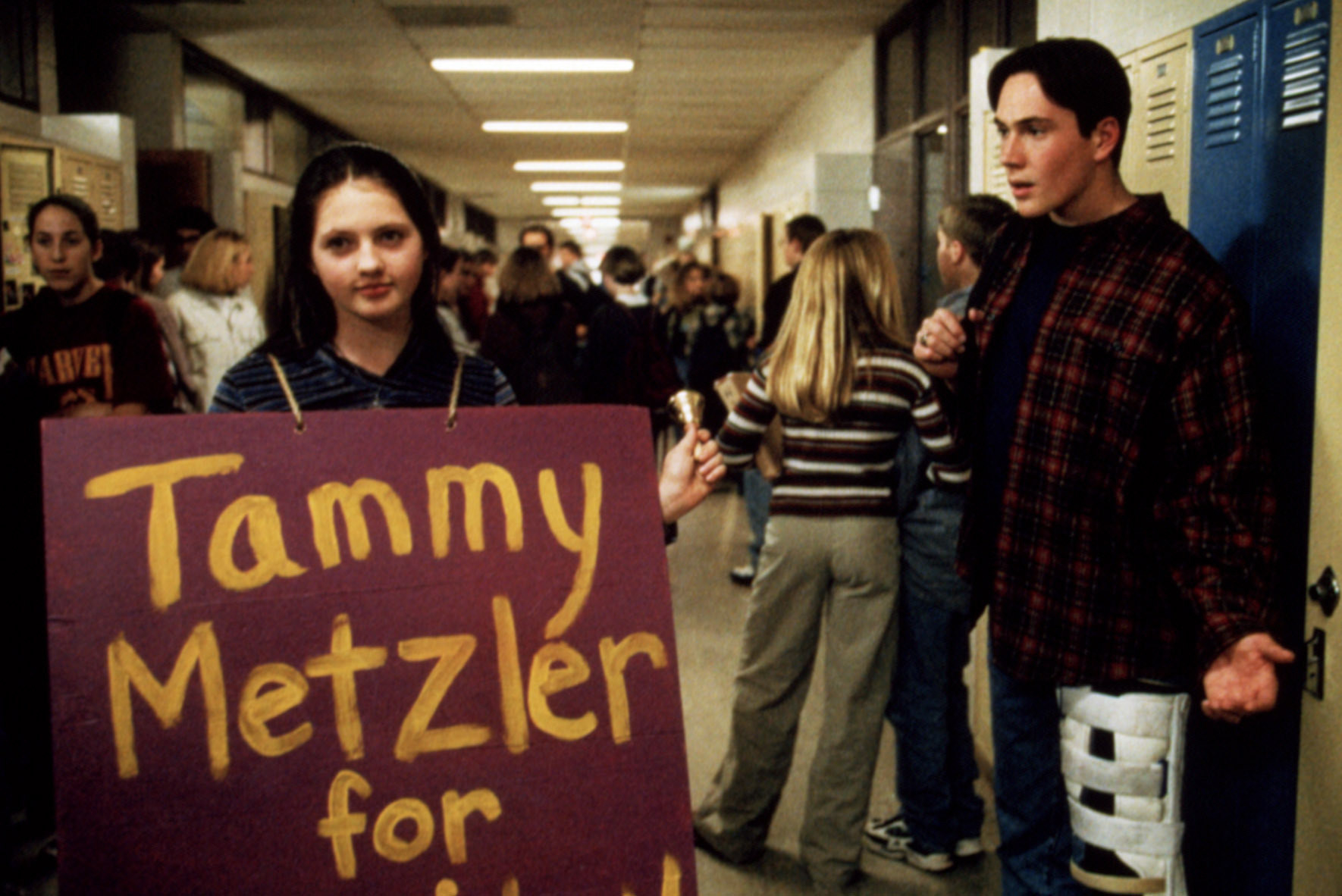 Jessica Campbell holds a campaign sign in the school hallway while Chris Klein looks on.