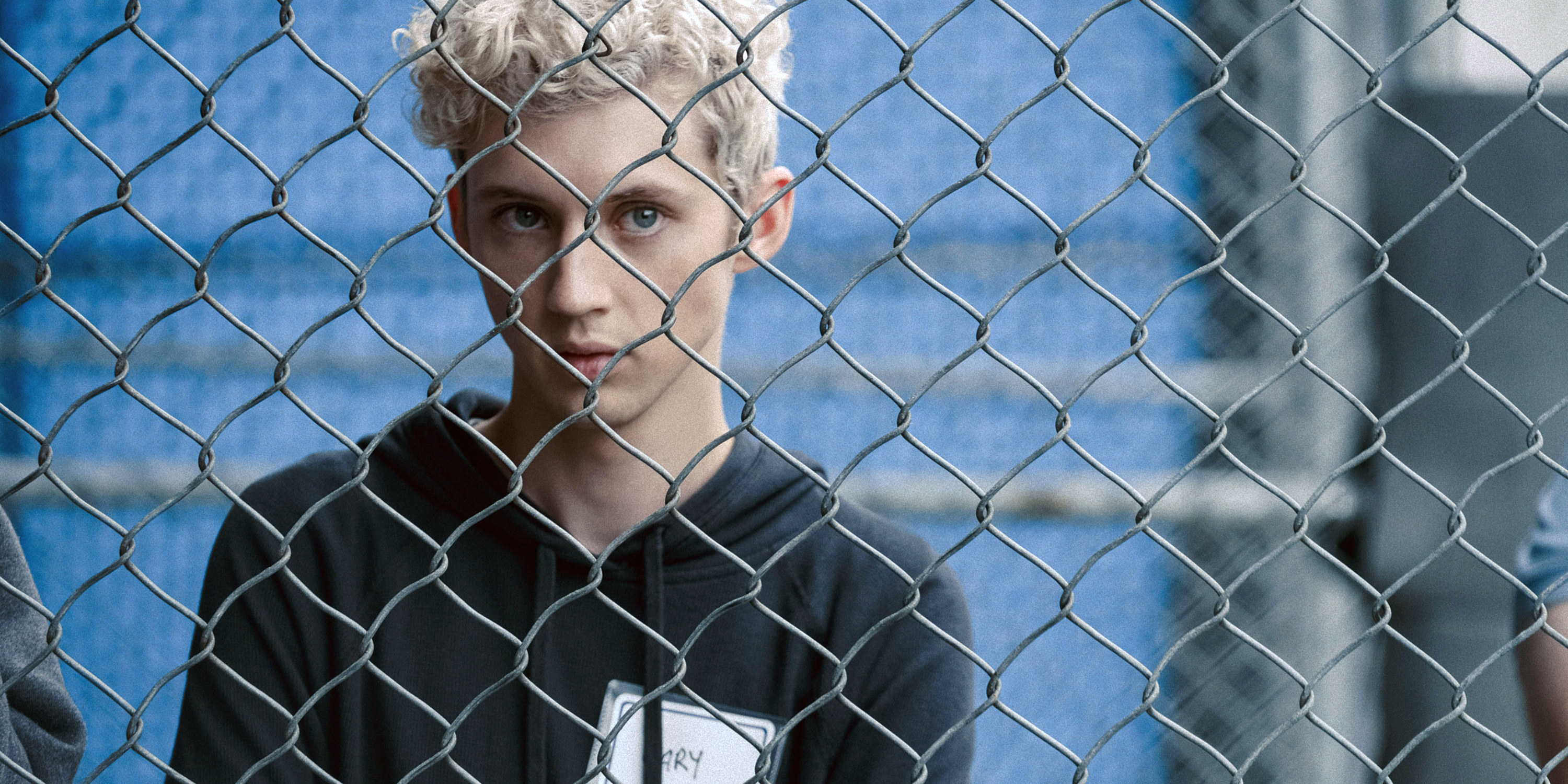 Troye Sivan looks out through a chainlink fence