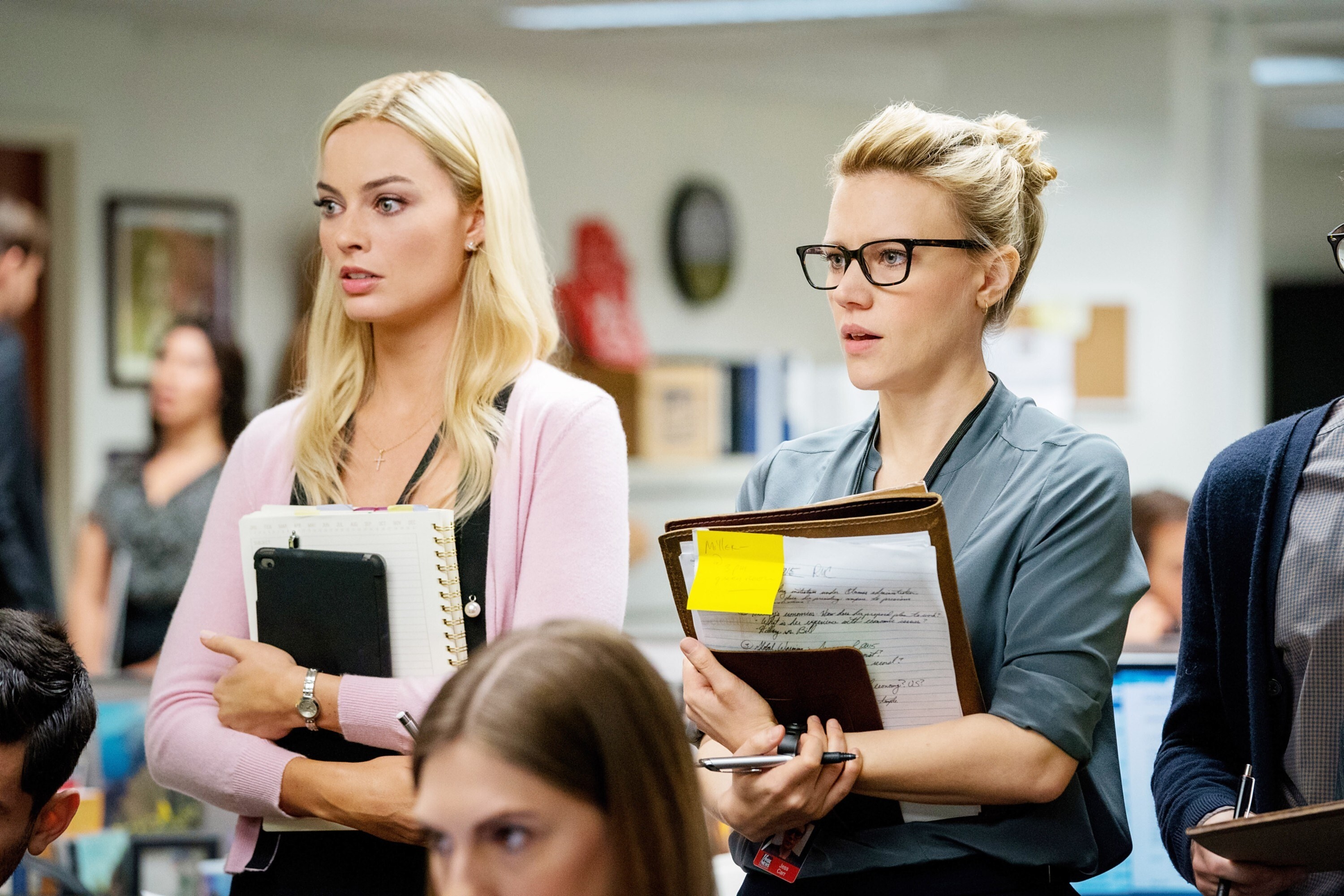 Margot Robbie and Kate McKinnon stand in a press room with notebooks