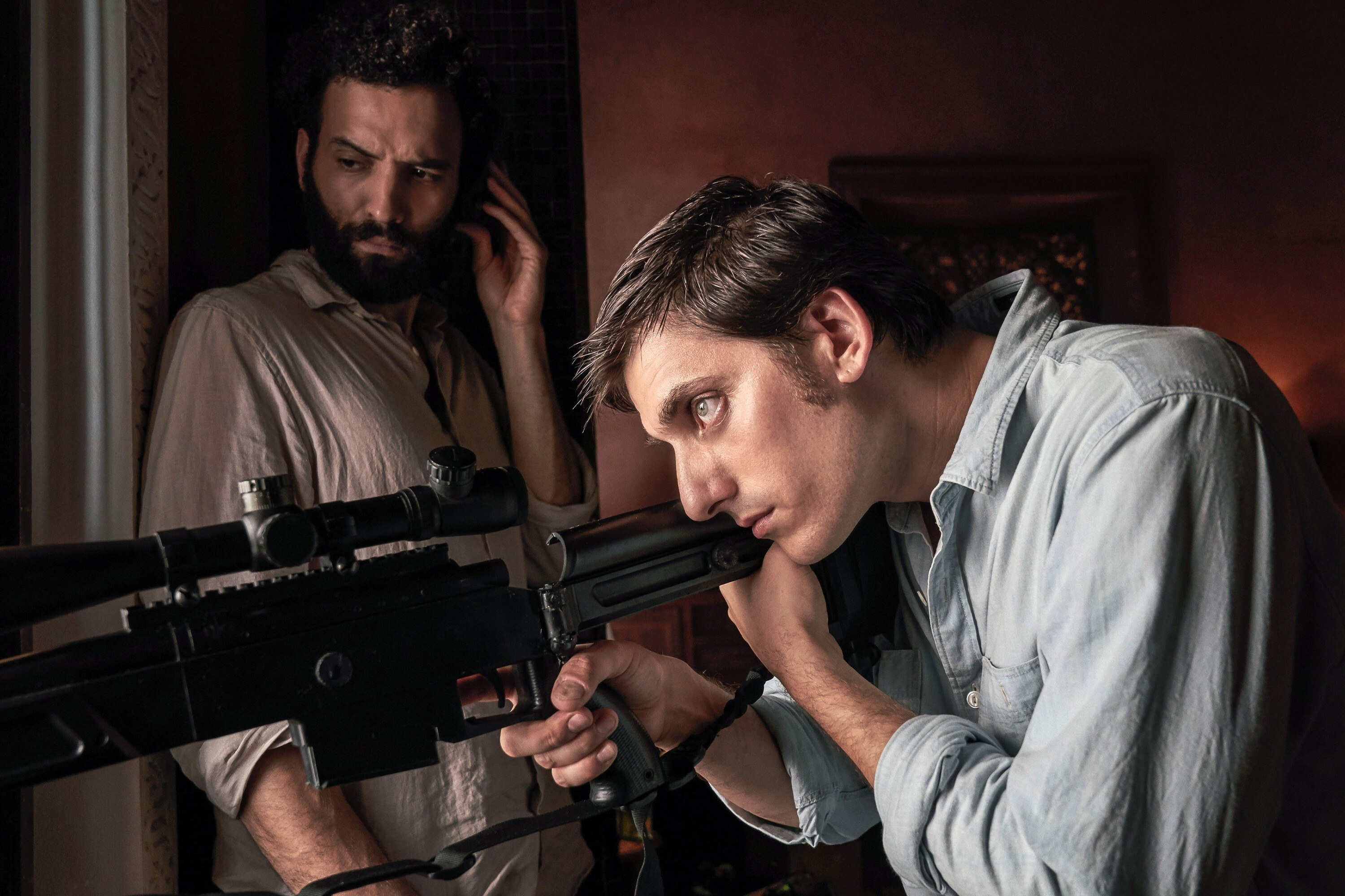 Luca Marinelli aims a gun out a window while Marwan Kenzari looks on