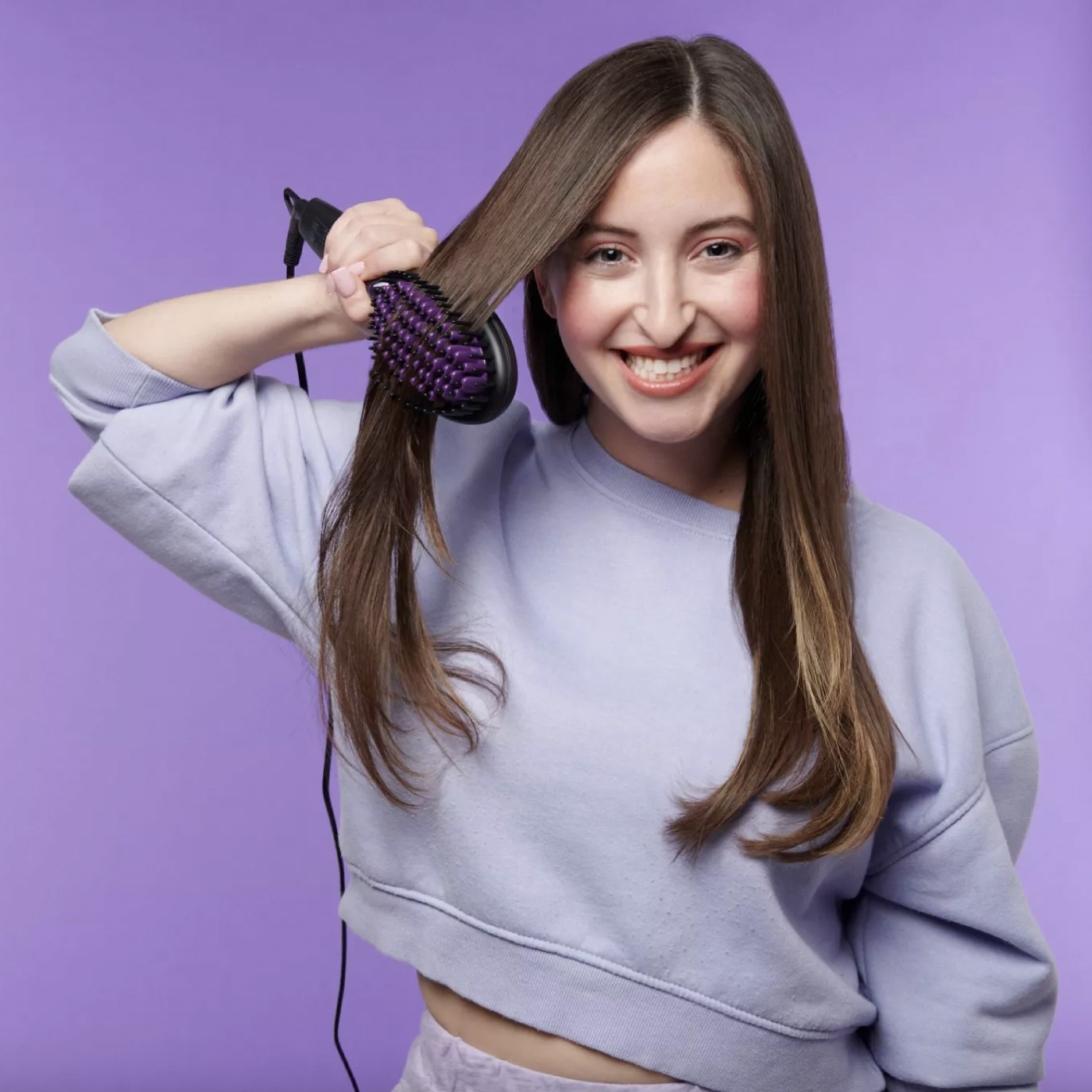 A woman straightening her hair with a straightener brush