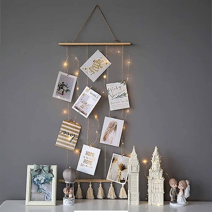 A wall hanging with attached wooden clips for hanging up pictures and notes. It&#x27;s laden with fairy lights.