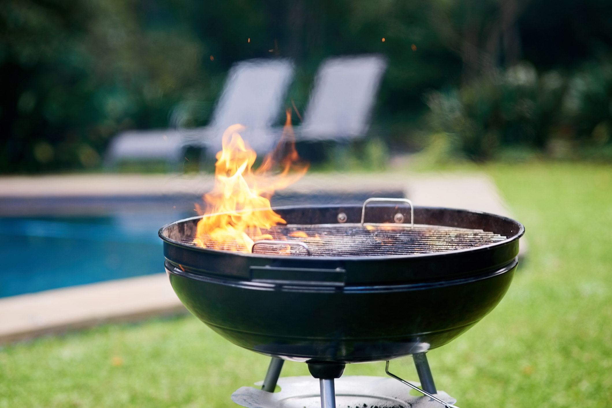 A lit grill outdoors by a pool.