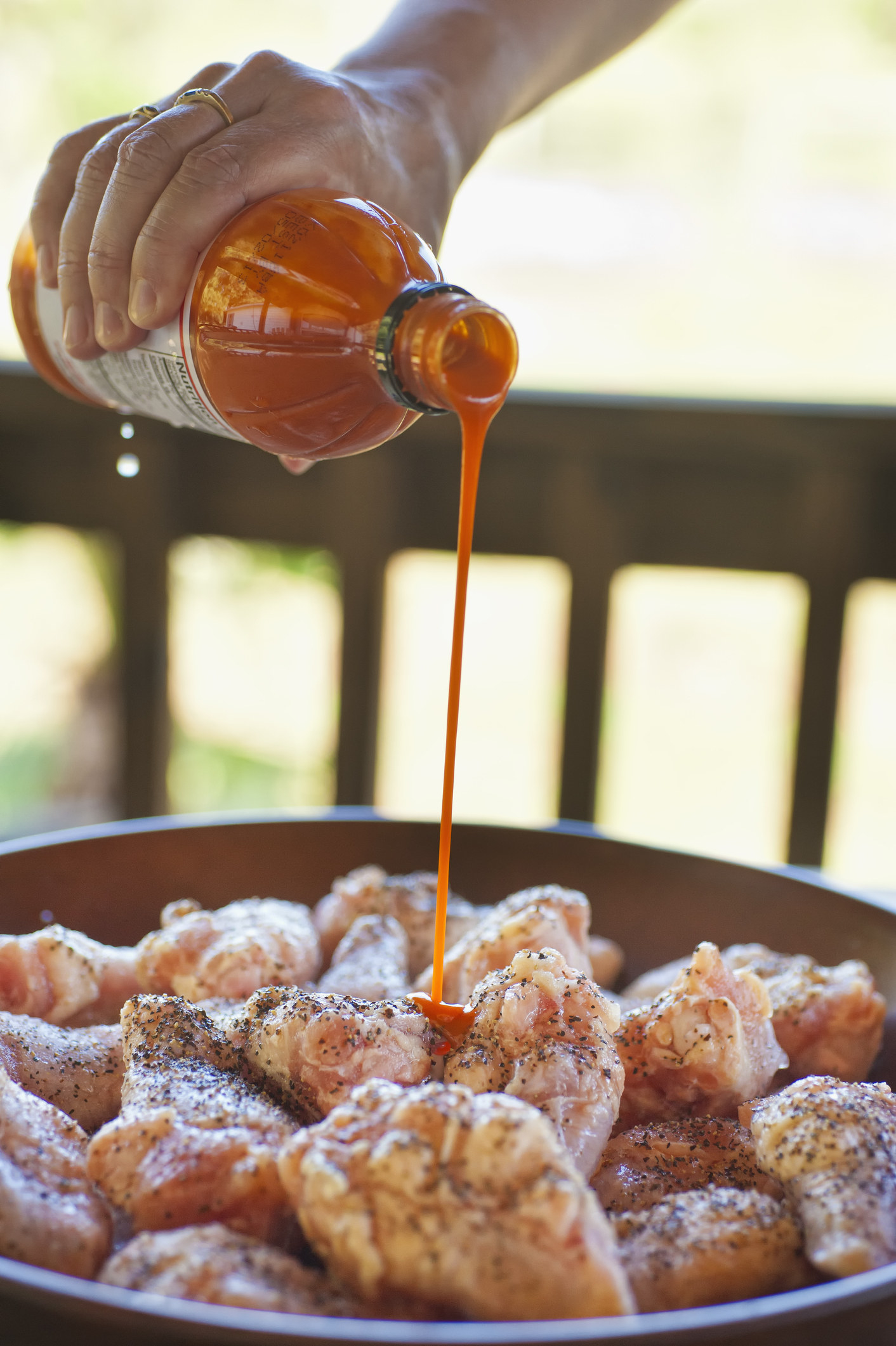 Pouring hot sauce onto chicken wings.