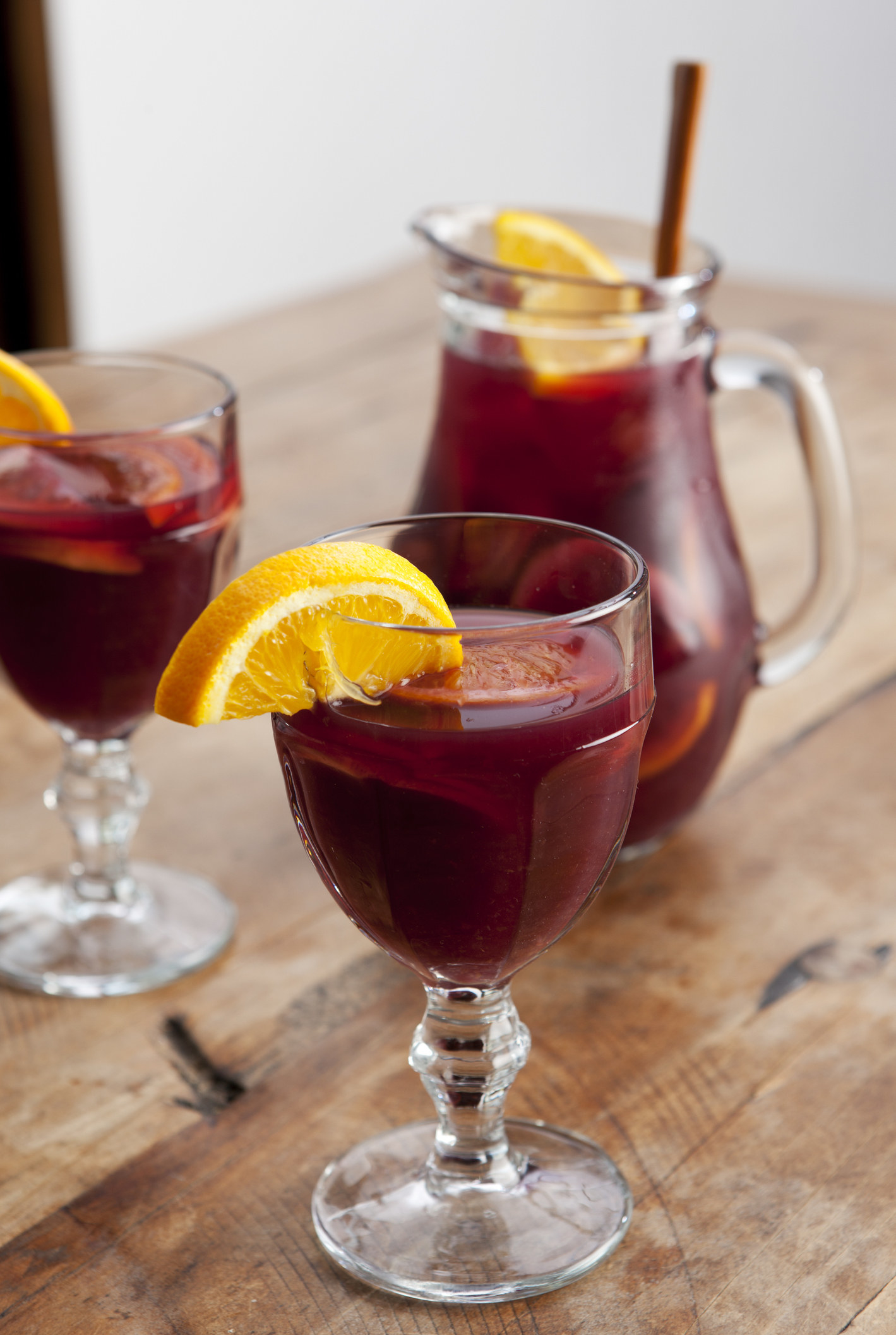 Two glasses of sangria next to a pitcher of Sangria on a wooden table