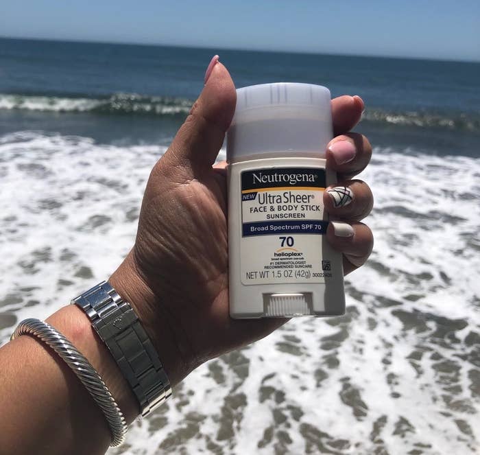 reviewer holding up a tube of neutrogena sunscreen at the beach