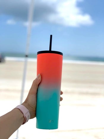 reviewer photo of a person holding up a two toned tumbler at the beach
