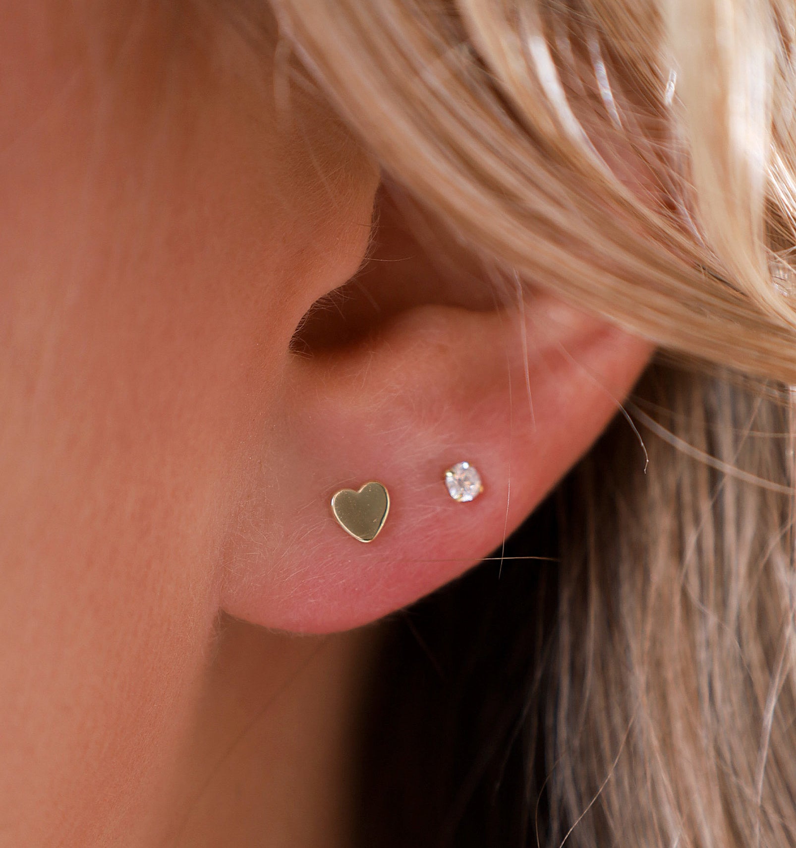 A close-up of a heart-shaped stud earring in someone's ear lobe