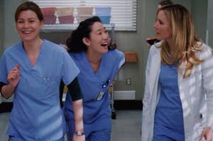 Meredith Grey smiles as she swings her arms back and forth, Cristina Yang is bent over laughing, and Lexie Grey has her head turned towards both of them with a frustrated expression.