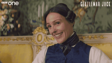 Anne Lister raises her eyebrows up and down in a flirty gesture while looking directly in the camera.