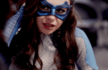 Nia Nal, wearing her blue Dreamer super suit and mask, looks up from the floor while running her hand down her face.
