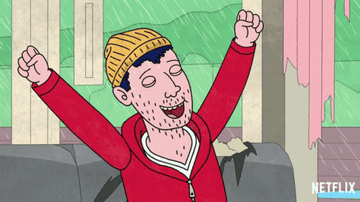 Todd, wearing a yellow beanie and red zipped up sweatshirt, has his arms in the air with his eyes closed in a cheer as rains pours down on him.