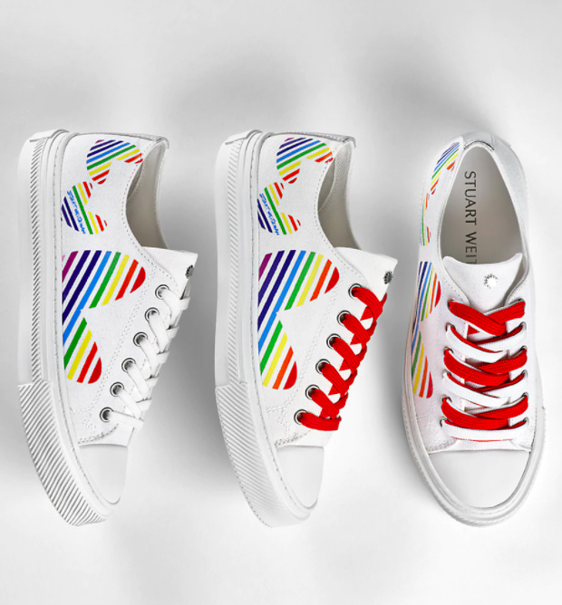 the sneakers which are white with big hearts on them with rainbow stripes, red and white shoelaces, and white shell-toes