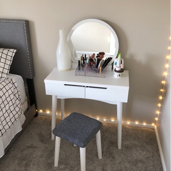 The white vanity with drawers and a round mirror attached, also a stool