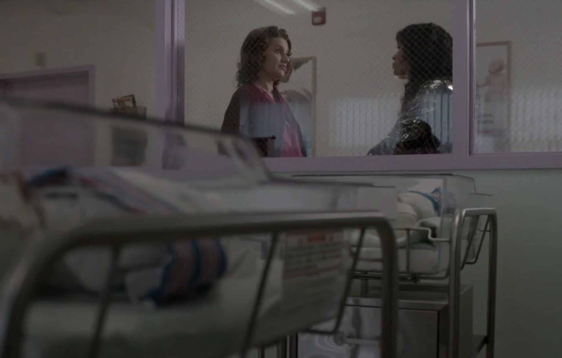 Nurse Judy standing with Blanca outside the window of the hospital&#x27;s maternity ward, two swaddled babies in hospital cribs in the foreground