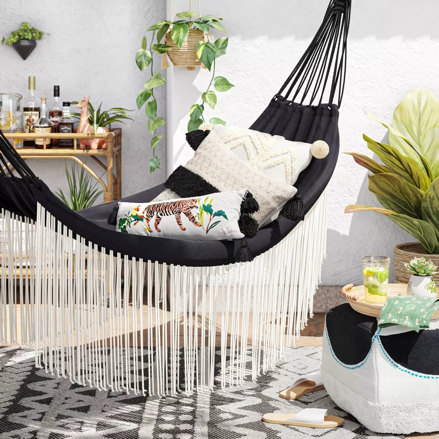 The black hammock with white fringe on either side in a backyard