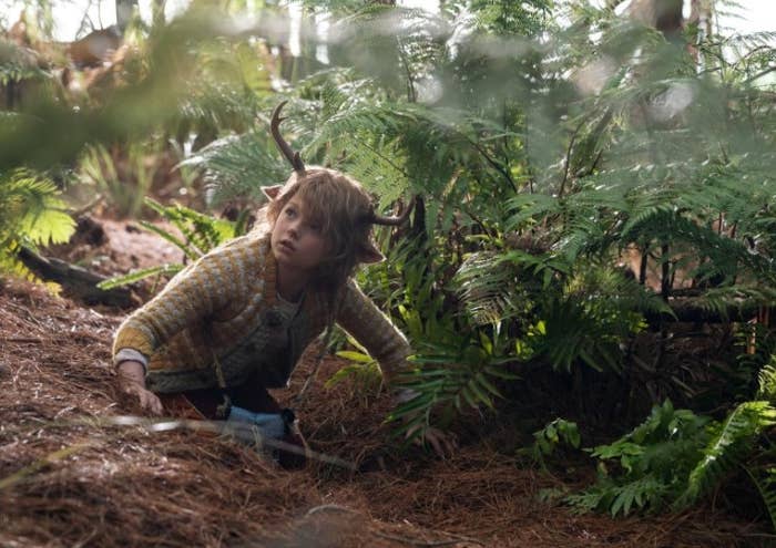 Sweet Tooth, a boy with deer horns, kneels in a forrest 